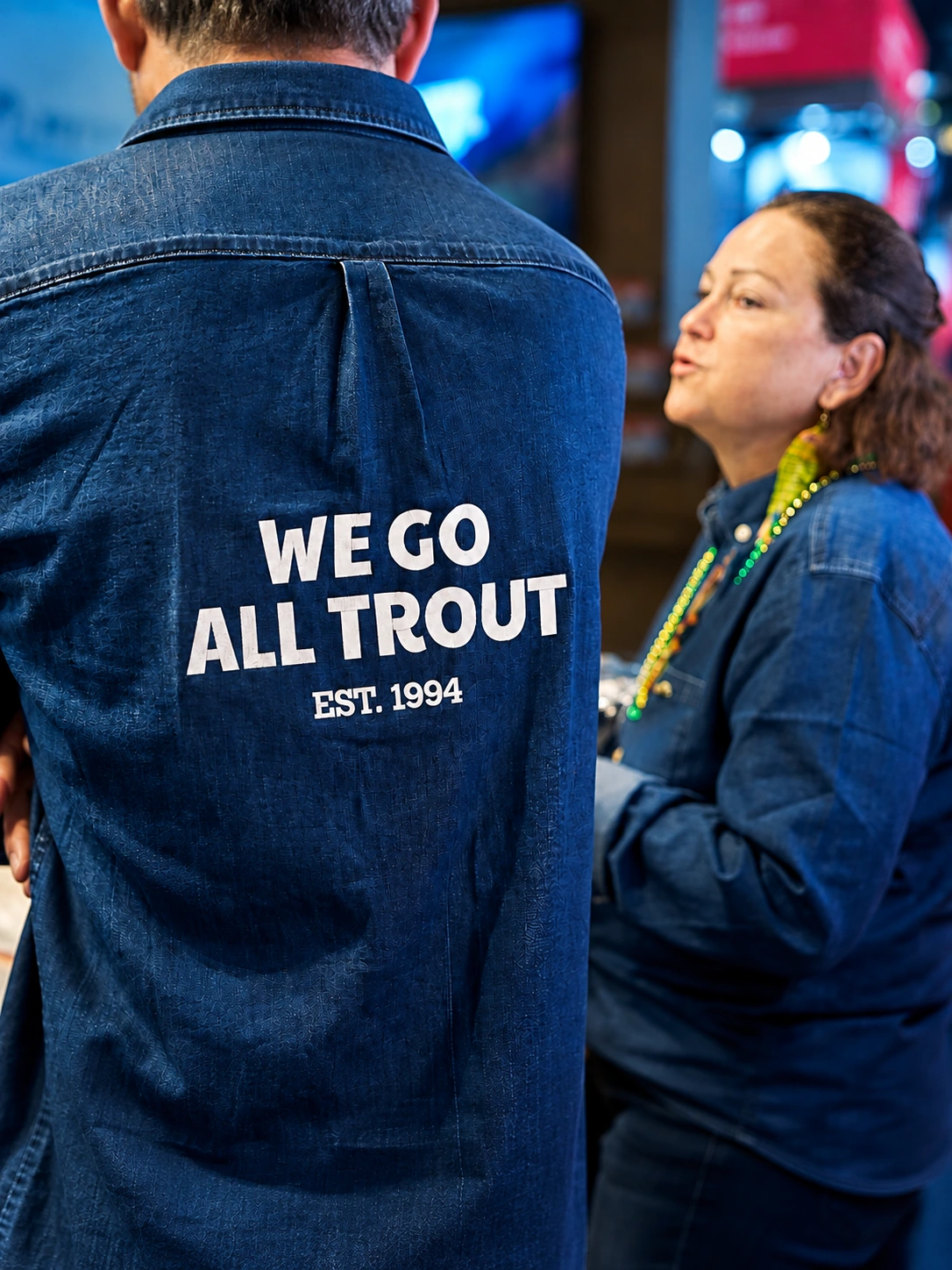 Close-up of a denim shirt with the slogan We go all trout, Est. 1994.
