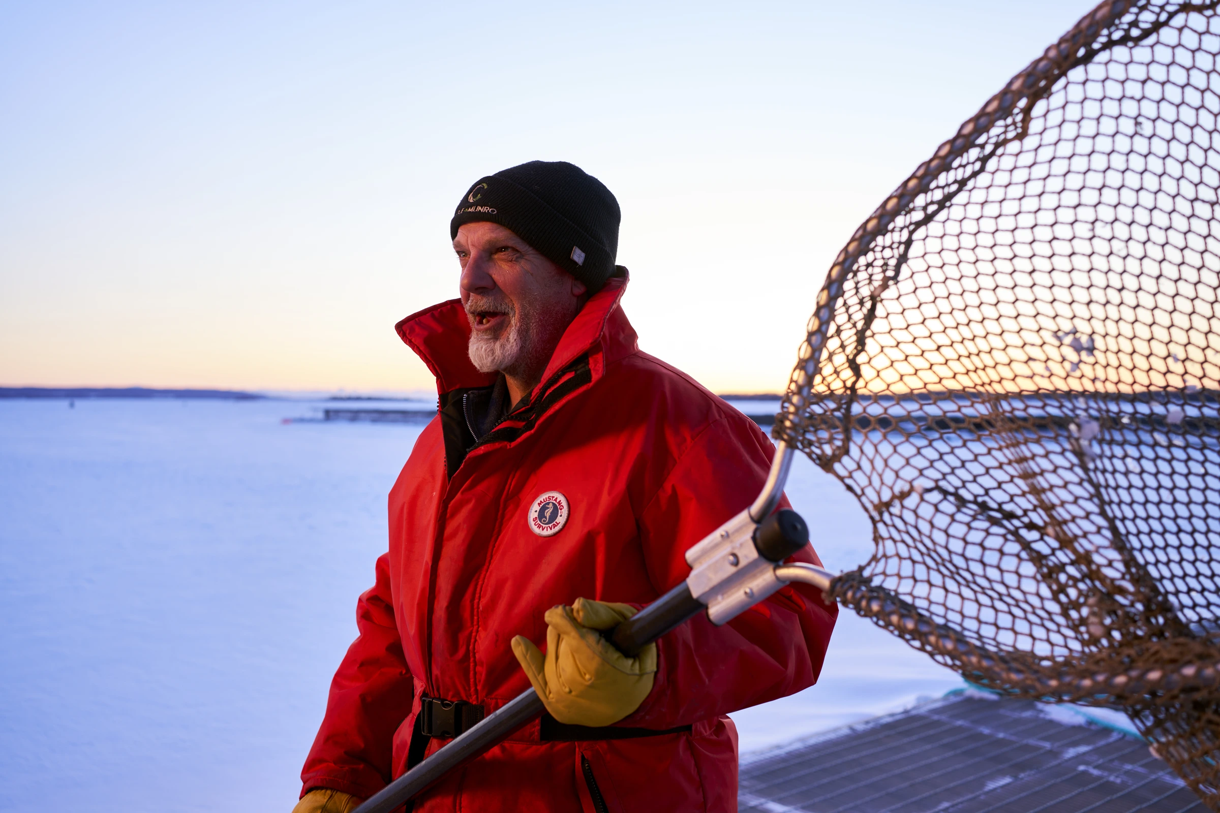 Cole Munro team member in a red winter jacket holding a fishing net beside the frozen lake.