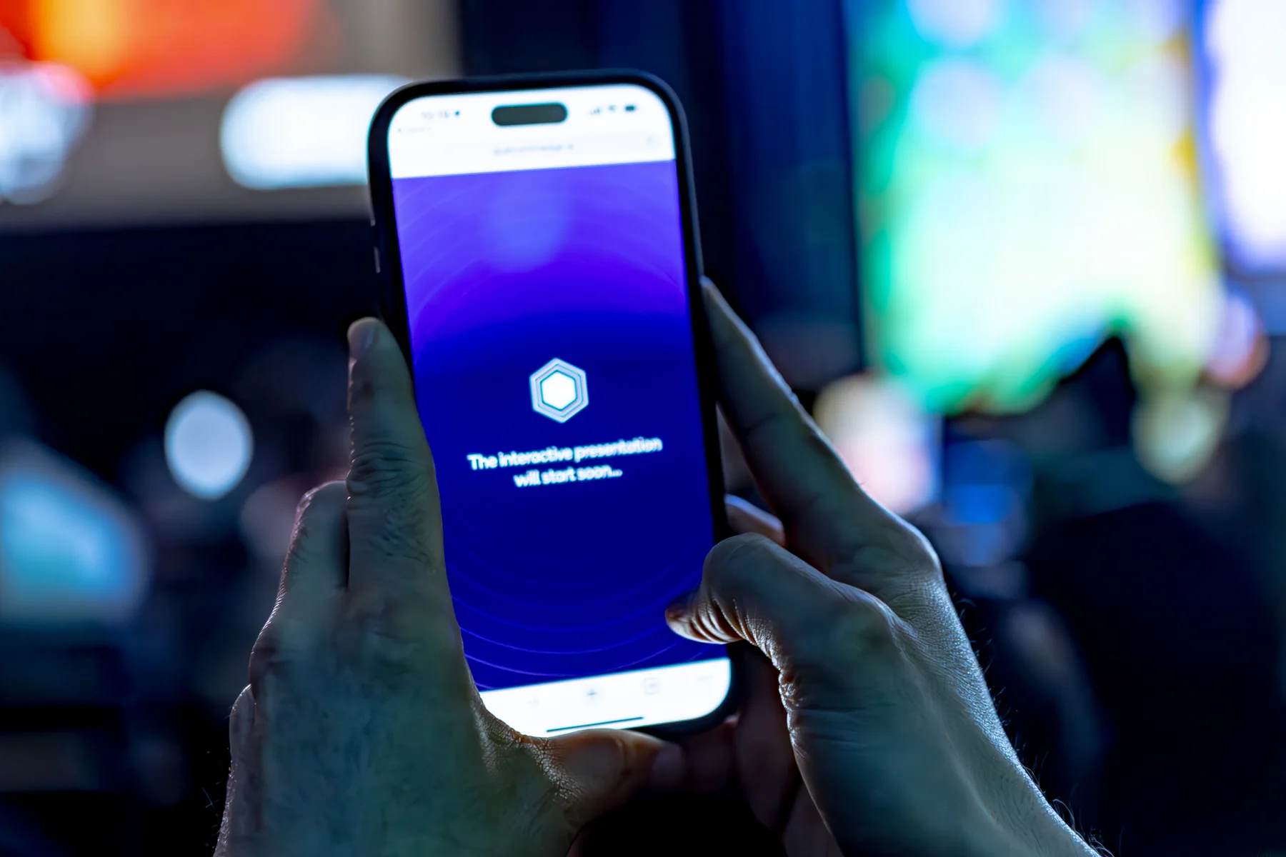 A phone in the audience displays the experience against the illuminated keynote stage.