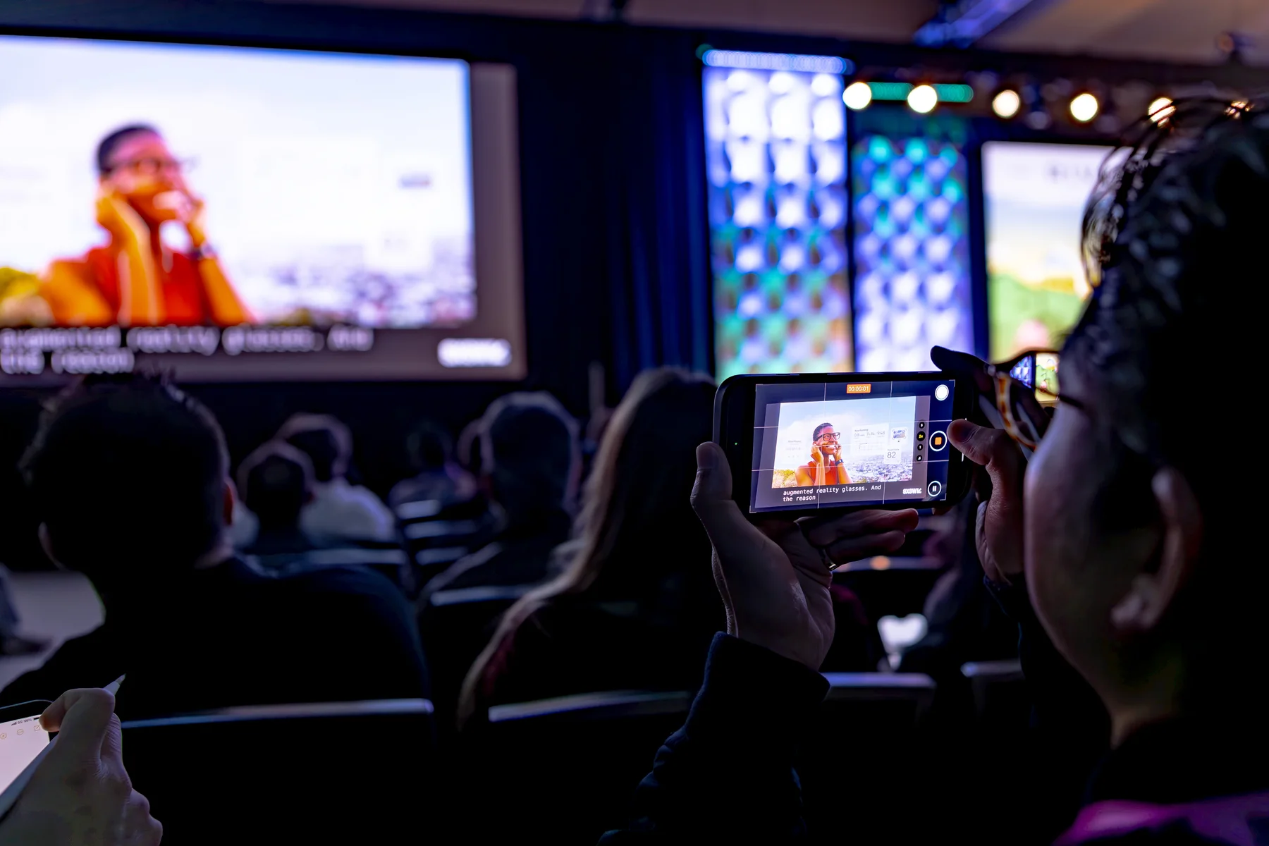 An attendee records the keynote while watching the stage.